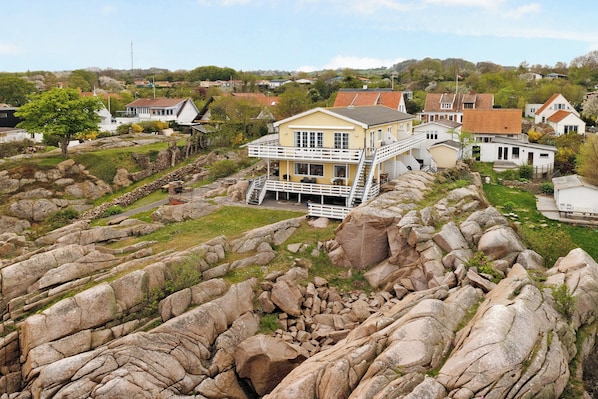 A two-story house with a balcony, surrounded by rocky terrain and other residential buildings.