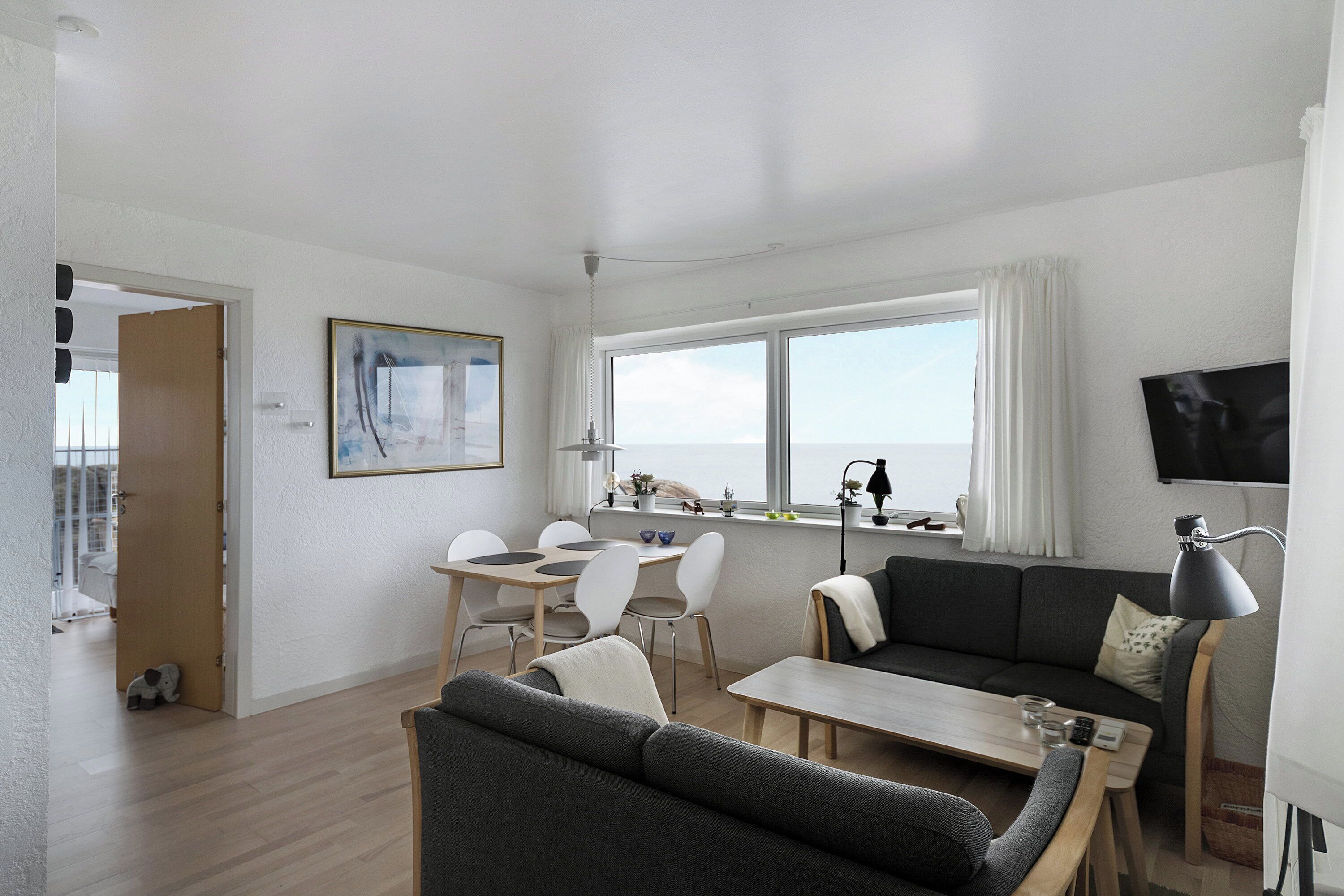 A modern living room with a sofa, dining table, and chairs, a TV, and a large window.