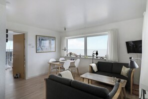 Una sala de estar moderna con sofá, mesa de comedor y sillas, televisor y un ventanal grande.