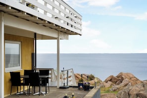 A seaside patio with a table and chairs, a white pergola, and a view of the ocean.