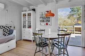 Une pièce comprenant une table à manger blanche, des chaises, un meuble avec des portes en verre, une bibliothèque et une fenêtre donnant sur l’extérieur.