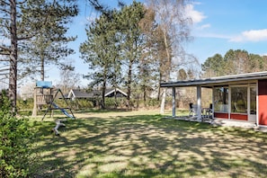 Un jardin avec une structure de jeux en bois, un patio couvert et une maison.