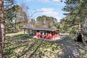 Un petit bâtiment d’un seul étage, doté d’un patio couvert, entouré d’arbres et d’une pelouse.