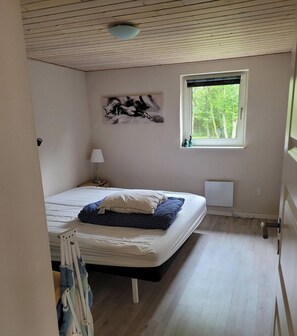 Une chambre à coucher comprenant un lit, une table de chevet, une lampe, une fenêtre donnant sur des arbres et un luminaire au plafond.