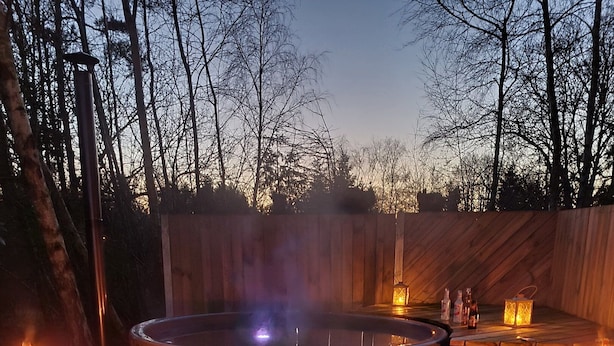 Un jacuzzi rodeado por una terraza de madera, con bancos y velas.