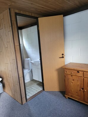 Une pièce avec un meuble en bois, un lavabo blanc et des toilettes visibles à travers une porte ouverte.
