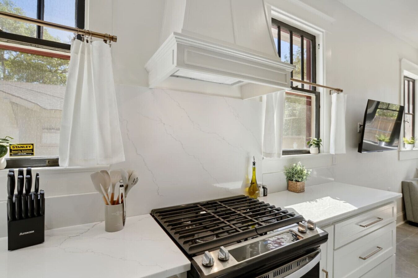 A modern kitchen with a gas stove, white marble countertops, and a window with a curtain.