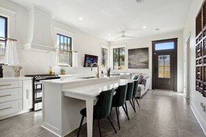A modern kitchen with white cabinetry, a central island, and a dining area with chairs. - Exquisite Garden District Haven, Walk to Dining (Baton Rouge)