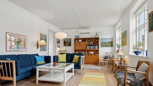 A living room with a blue sofa, white coffee table, wooden bookshelf, and a patterned rug. - Cozy holiday home in Marstal on Ærø (Marstal)