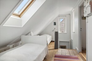 A room with a sloped ceiling, a skylight, two beds, a radiator, a trash bin, and a door leading to another room.