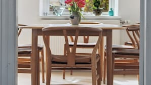 A dining area with a table and chairs, a window with a view of greenery, and a pendant light. - Cozy holiday home in Marstal on Ærø (Marstal)