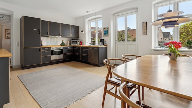 A modern kitchen with dark cabinets, a wooden dining table, and a large window. - Cozy holiday home in Marstal on Ærø (Marstal)