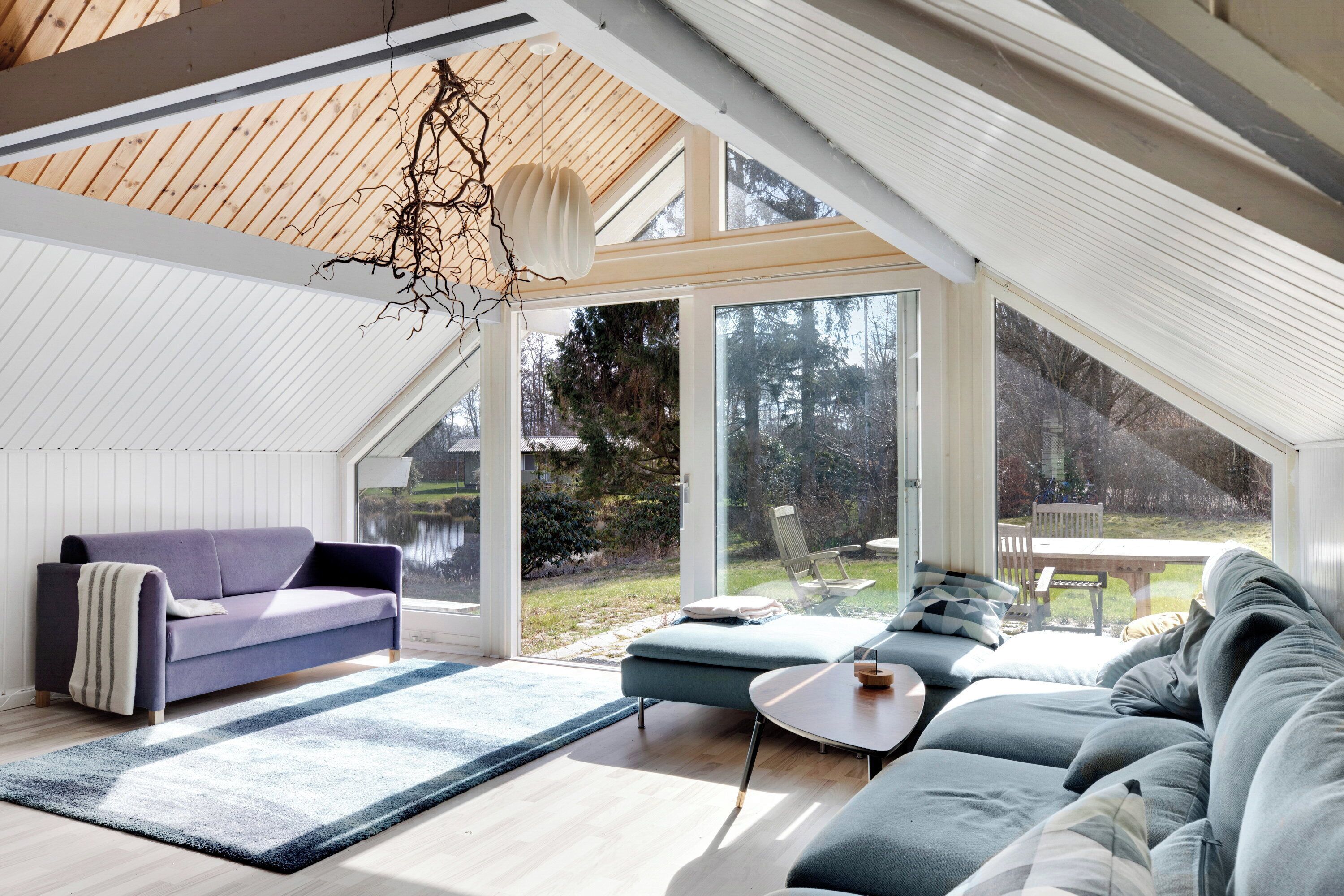 Ein modernes Interieur mit hoher Decke, großen Fenstern, einer Couch und einem Essbereich.