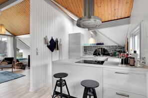 A modern kitchen with white cabinetry, a central island, two bar stools, and a hanging light fixture.