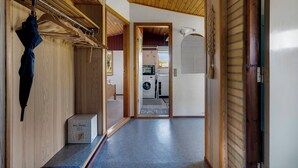 Un corridoio con soffitto in legno, un'asciugaio a parete, una porta che dà su un'area lavanderia e un pavimento piastrellato.