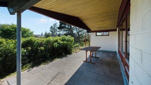 Un'area patio esterna coperta con un tavolo e panche, immersa nel verde e adiacente a un edificio con finestre.