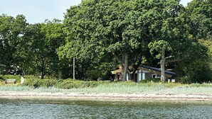 Ein Haus am See, umgeben von Bäumen und mit einer Bank.