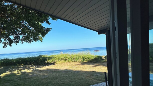 Blick von einer überdachten Terrasse auf einen Strand bei blauem Himmel.