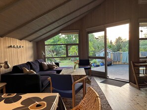 A cozy room with a wooden ceiling, a sofa, a dining table, and large windows offering a view of the outdoors.