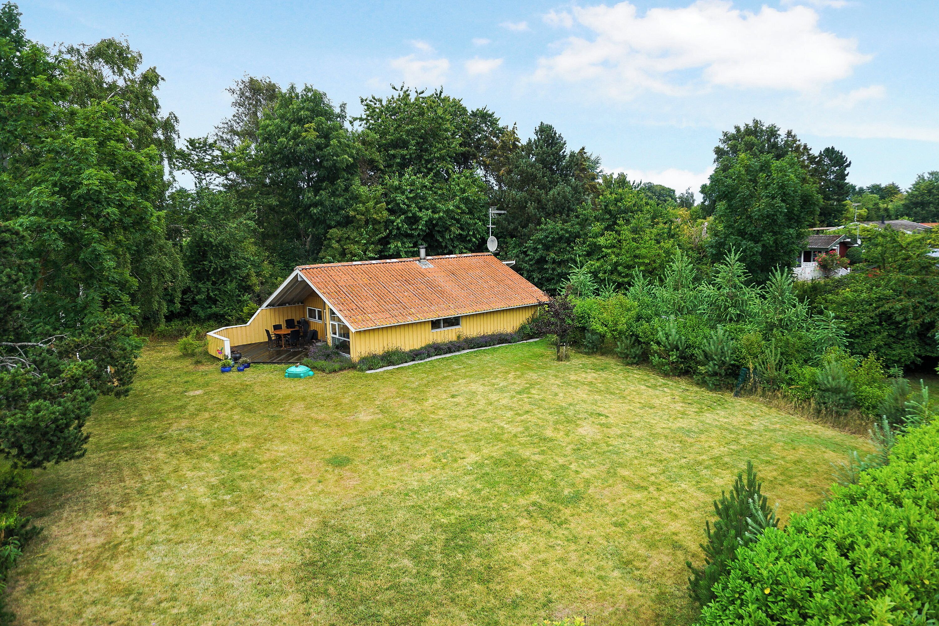 A yellow house with a red roof surrounded by a grassy yard and dense trees.
