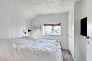 Un dormitorio con cama, ventana con vistas, luz empotrada en la pared y puerta.