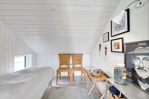 A bedroom with a bed, two wooden chairs, a table with a jar of candies, and framed pictures on the wall.