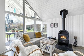 A cozy room with a sofa, a table, a white furry chair, a fireplace, and large windows.