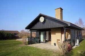 A modern house with a brick chimney, a covered porch, and a clear sky.