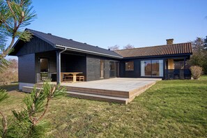 A modern house with a covered porch, a small deck, and a well-maintained lawn.