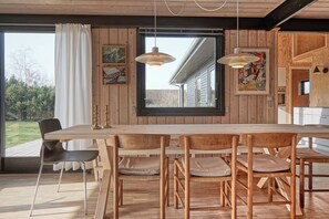 Un espace repas avec une table et des chaises en bois, de grandes fenêtres et des œuvres d’art accrochées aux murs.
