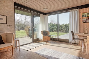 Un salon moderne comprenant un canapé, un fauteuil, une table à manger et donnant sur un jardin grâce à de grandes portes-fenêtres coulissantes.