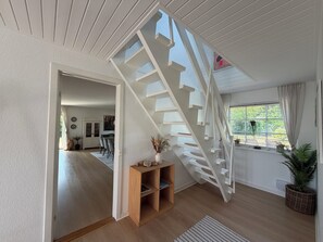 Ein modernes Interieur mit einer Holztreppe, einem Essbereich und einem Fenster mit Pflanzen.
