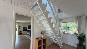 A modern interior with a wooden staircase, a dining area, and a window with plants.