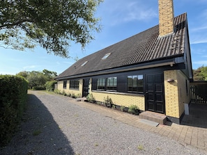 A two-story house with a tiled roof, a chimney, and a gravel driveway.