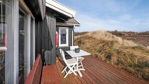 A wooden deck with a table and chairs, a small window, and a view of dunes. - Holiday idyll between fjord and sea (Hvide Sande)