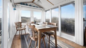 A sunroom with a wooden table and chairs, large windows, and a hanging light fixture. - Holiday idyll between fjord and sea (Hvide Sande)