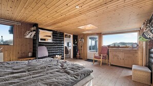 A log cabin interior with a bed, wooden walls, a dining area, and a view of the outdoors. - Holiday idyll between fjord and sea (Hvide Sande)
