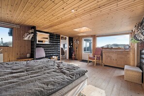 A log cabin interior with a bed, wooden walls, a dining area, and a view of the outdoors.