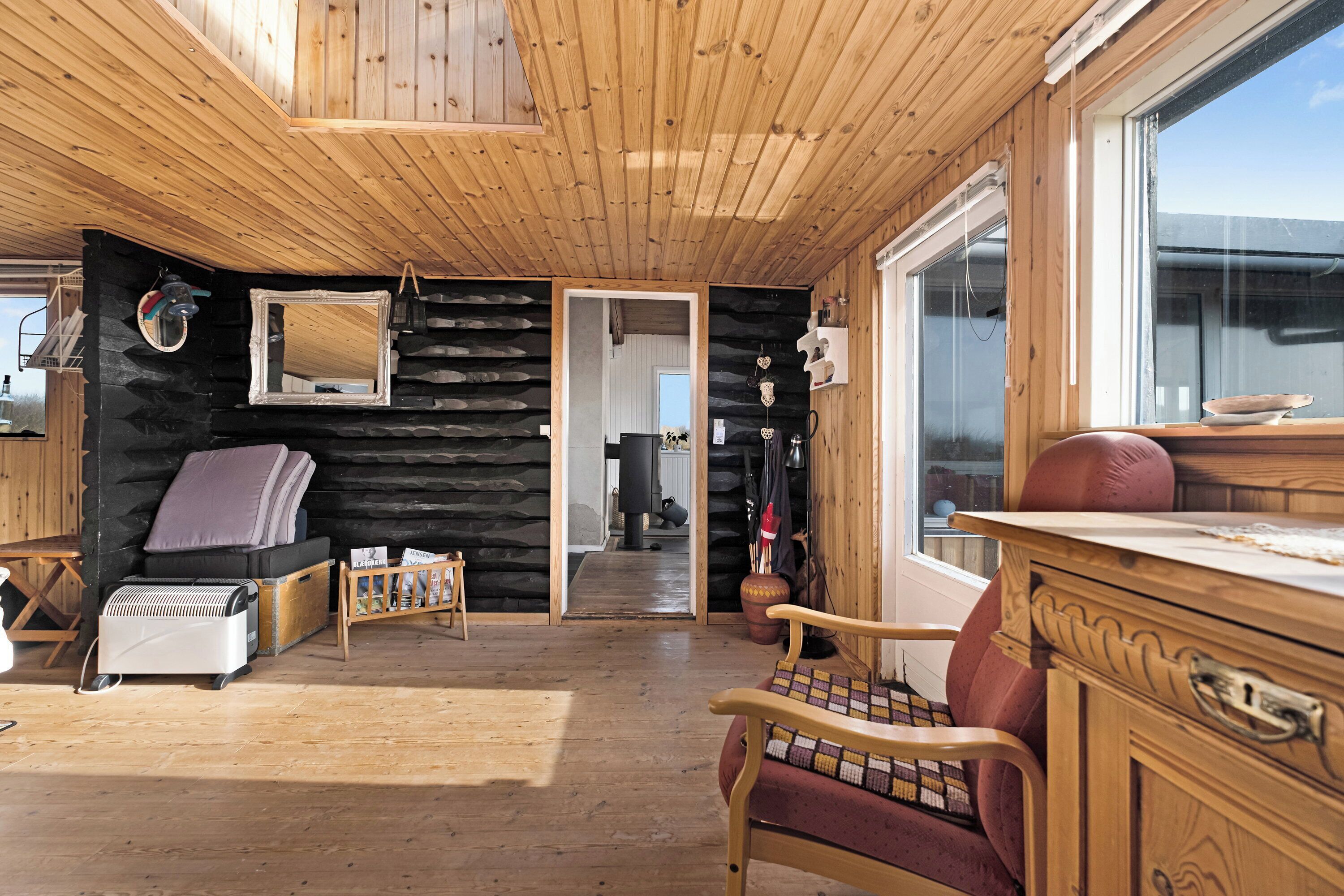 A log cabin interior with a wooden ceiling, a fireplace, a dining area, and a large window.