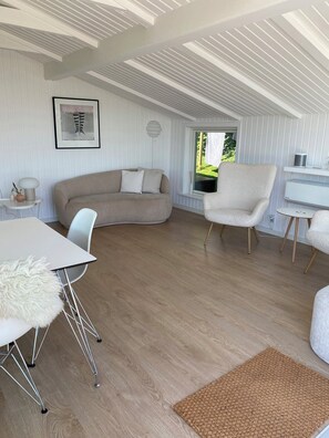 Ein modernes Interieur mit einer gebogenen Couch, einem weißen Esstisch, einem weißen Sessel und Blick auf Grünflächen.