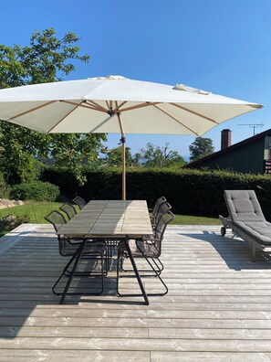 Un terrazzo in legno con tavolo, sedie, un ombrellone e una poltrona da relax.