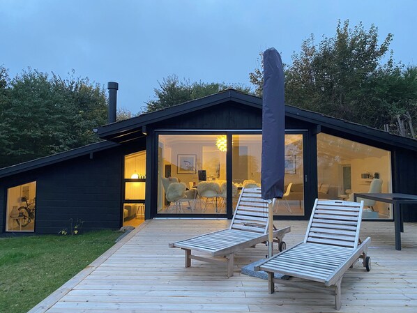 Ein modernes Haus mit einer großen Glasdoor, einer Holzdiele und zwei Liegestühlen.
