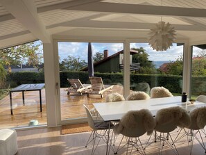 Un interno moderno con un'ampia porta vetrata che si apre su una terrazza esterna, un tavolo da pranzo bianco e poltrone accoglienti.
