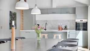 A modern kitchen with a central island, pendant lighting, and a dining area with a long table and chairs. - Newly built summer house full of luxury (Hals)