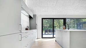 A modern kitchen with white cabinetry, a wooden floor, and a view of an outdoor deck through a glass door. - Newly built summer house full of luxury (Hals)
