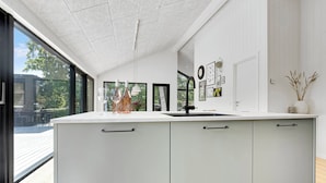 A modern kitchen with a large island, a sink, and a view of the outdoors. - Newly built summer house full of luxury (Hals)