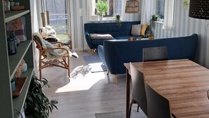 A living room with a blue sofa, a wooden dining table, and a wicker chair. - Beautiful holiday home on an undisturbed plot (Rødby)