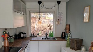 A compact kitchen with white cabinets, a built-in dishwasher, a sink with a window above, and hanging pendant lights. - Beautiful holiday home on an undisturbed plot (Rødby)