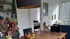 A wooden dining table with a vase of flowers, a fruit bowl, and a bench with a fur throw. - Beautiful holiday home on an undisturbed plot (Rødby)