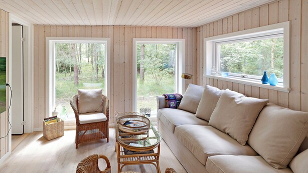 A room with a wooden ceiling, two large windows, a wicker chair, a sofa, and a glass-top table. - Charmantes Sommerhaus in der Nähe eines fantastischen Sandstrandes (Åkirkeby)